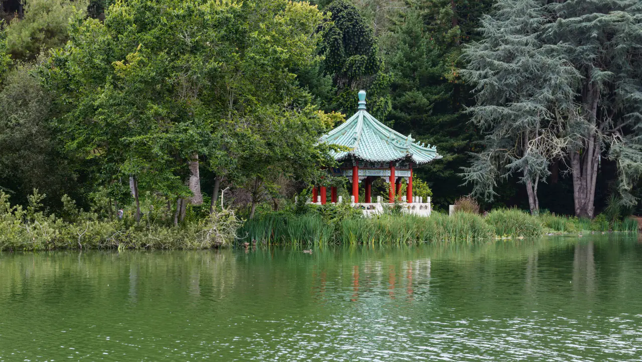 The red and green Chinese Pavilion on the shore of Blue Heron Lake, reflected in the water