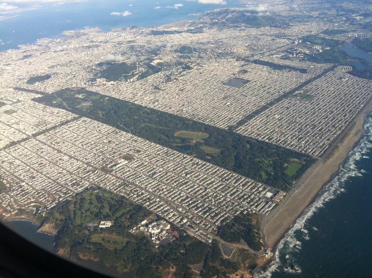 Aerial view of the long green rectangle of Golden Gate Park between city blocks, reaching the ocean
