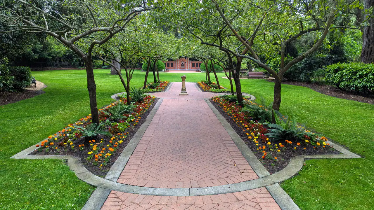 A brick path leading between flowerbeds and trees to the gates of the Shakespeare Garden